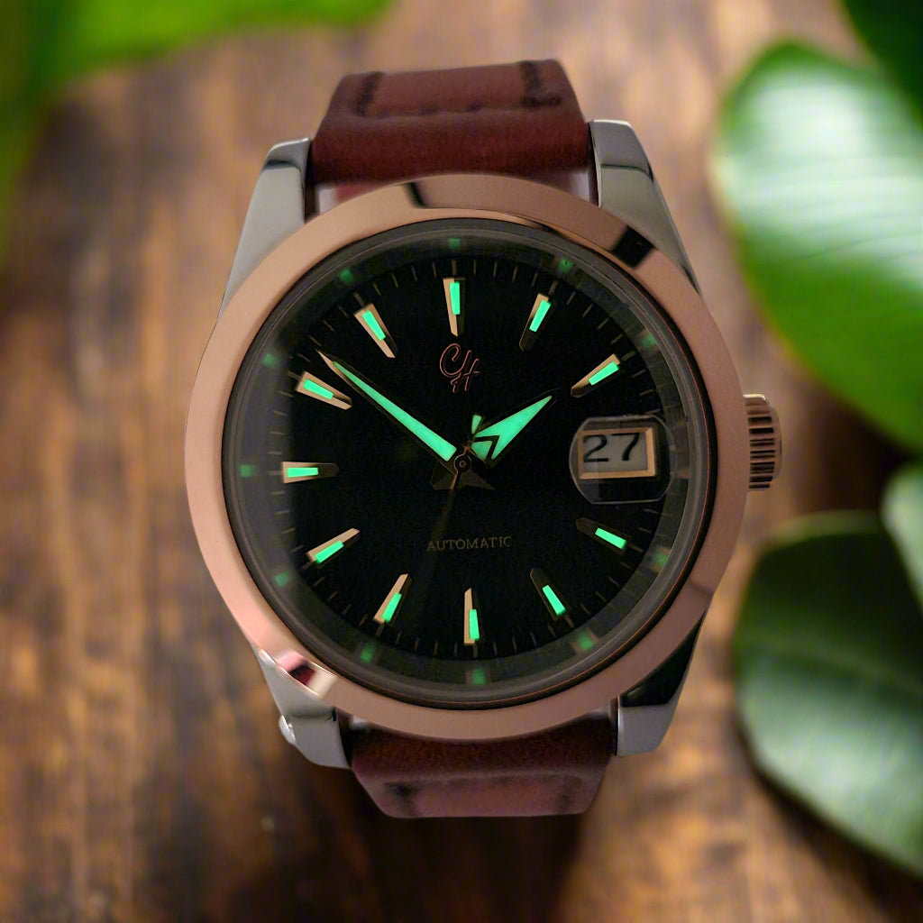 Watch with a brown leather strap and black face on a wooden surface with green leaves.