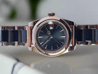 Luxury watch with a rose gold case and black ceramic bracelet on a light blue background