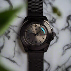 Black wristwatch with a dark mesh band on a black background