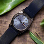 Watch with a blue strap on a textured surface with green leaves