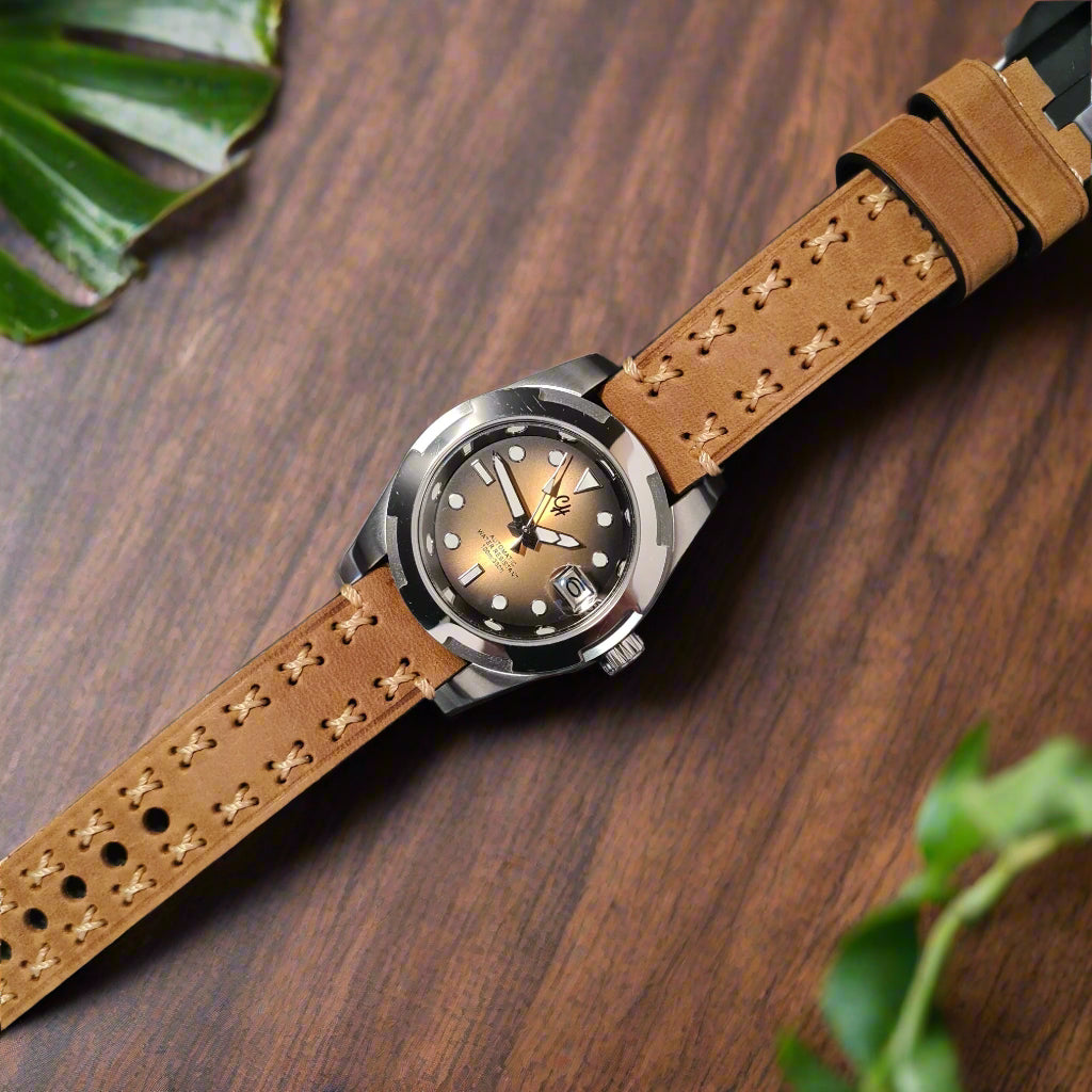 A statement of rugged sophistication and warm tones. This watch features a gradient brown dial with a sunray effect, transitioning from lighter amber in the centre to deeper brown at the edges, accented by luminous white dot markers, triangular indices at key positions, and crisp white hands, including a date window at 3 o'clock. Encased in a polished silver stainless steel case, paired with a tan leather strap featuring light beige cross-stitching for a durable, earthy look. 