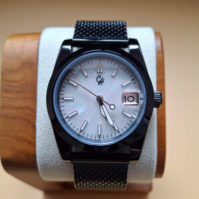 Black wristwatch with a black mesh band on a wooden display block.