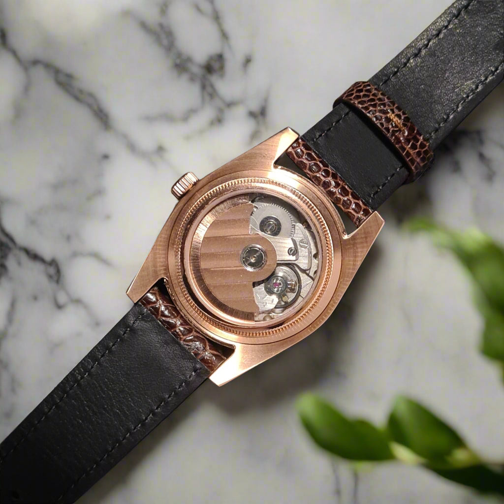 Rose gold watch with black leather strap on a gray background