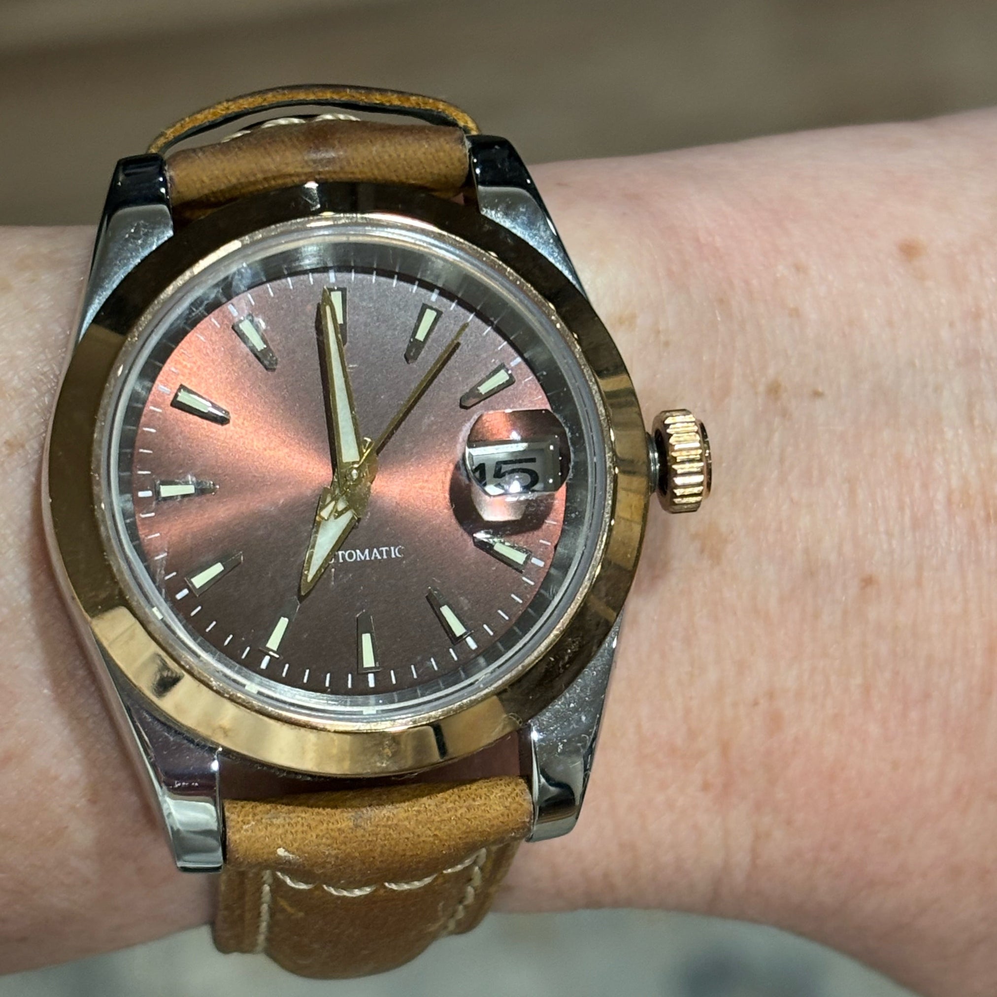 Watch with brown leather strap and metallic case on wrist