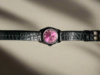 Watch with a pink face and black strap on a dark background