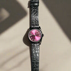 Watch with a black strap and pink face on a dark gray background