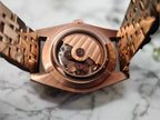 Rose gold watch with open face revealing mechanical components on a marble background